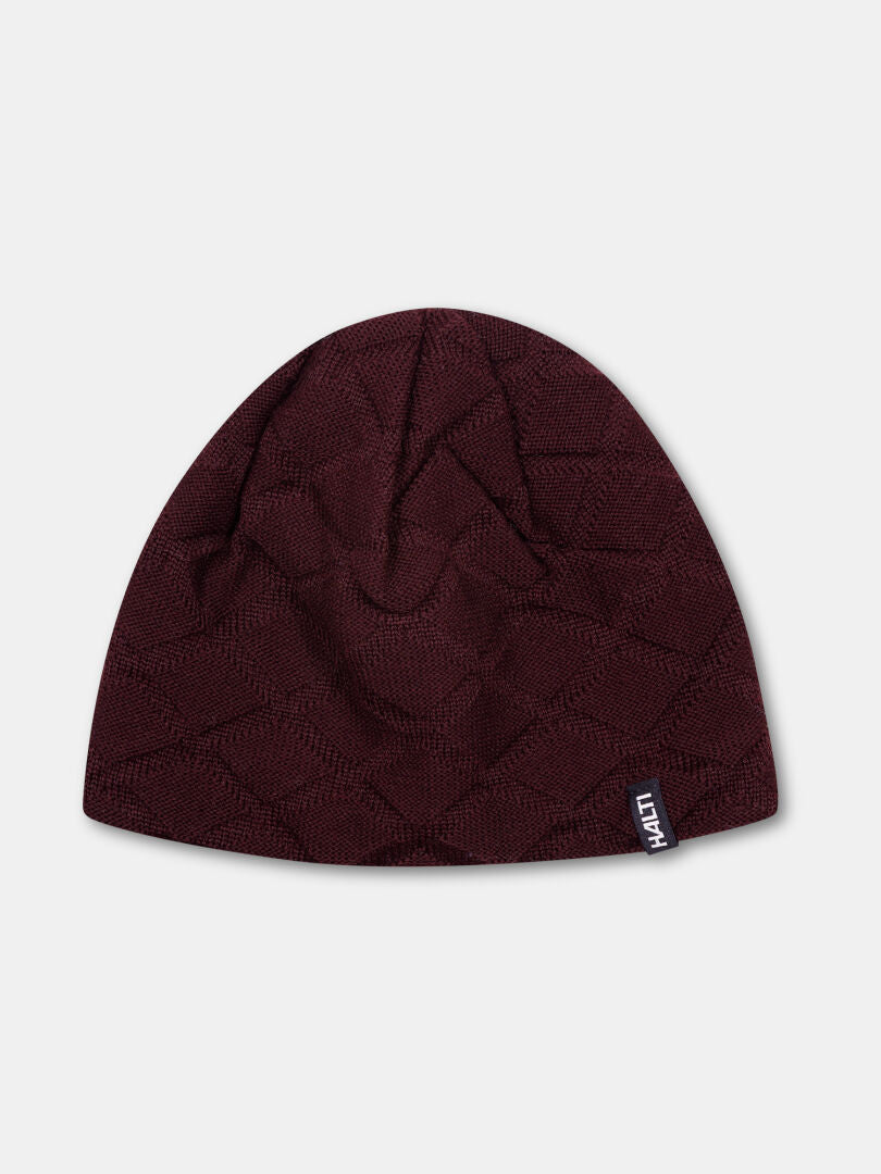 The Crostie Merino Beanie by Halti is a maroon wool hat with a textured pattern and a small black-and-white side tag.