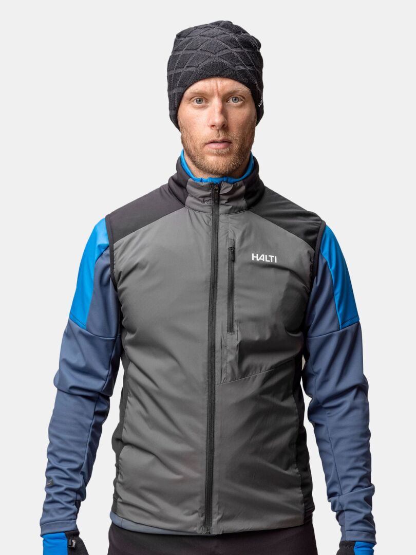 A man in a gray and blue jacket wears Halti's Crostie Merino Beanie and gloves against a plain background.