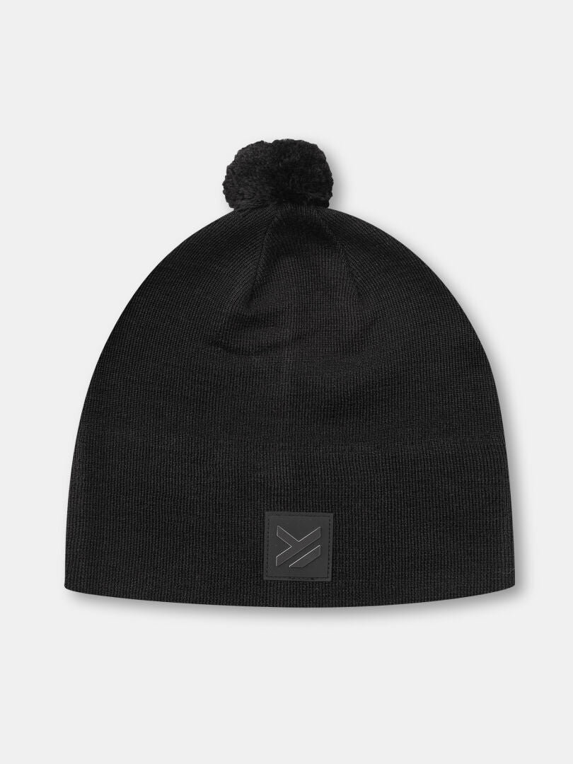 Halti Pilke Beanie: black merino knit with pom-pom and patch, ideal for winter sports or skiing.