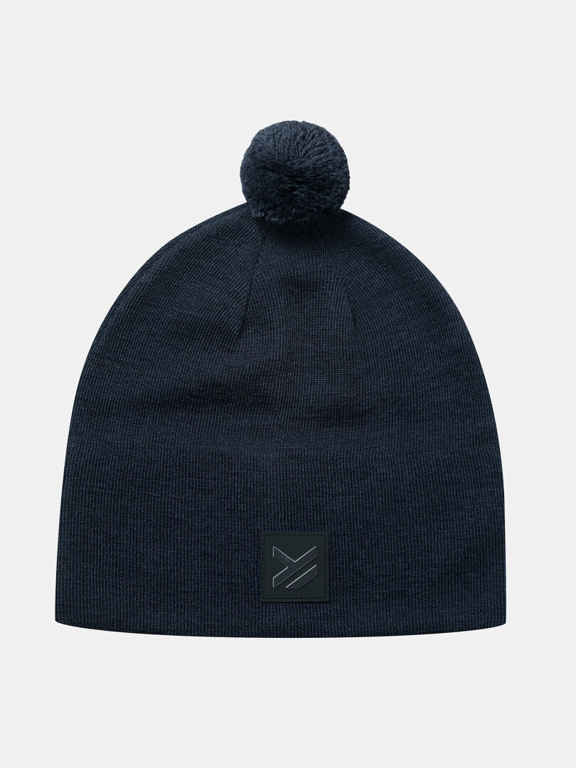 Halti Pilke Beanie: navy merino blend with pom-pom and square black patch on the front.
