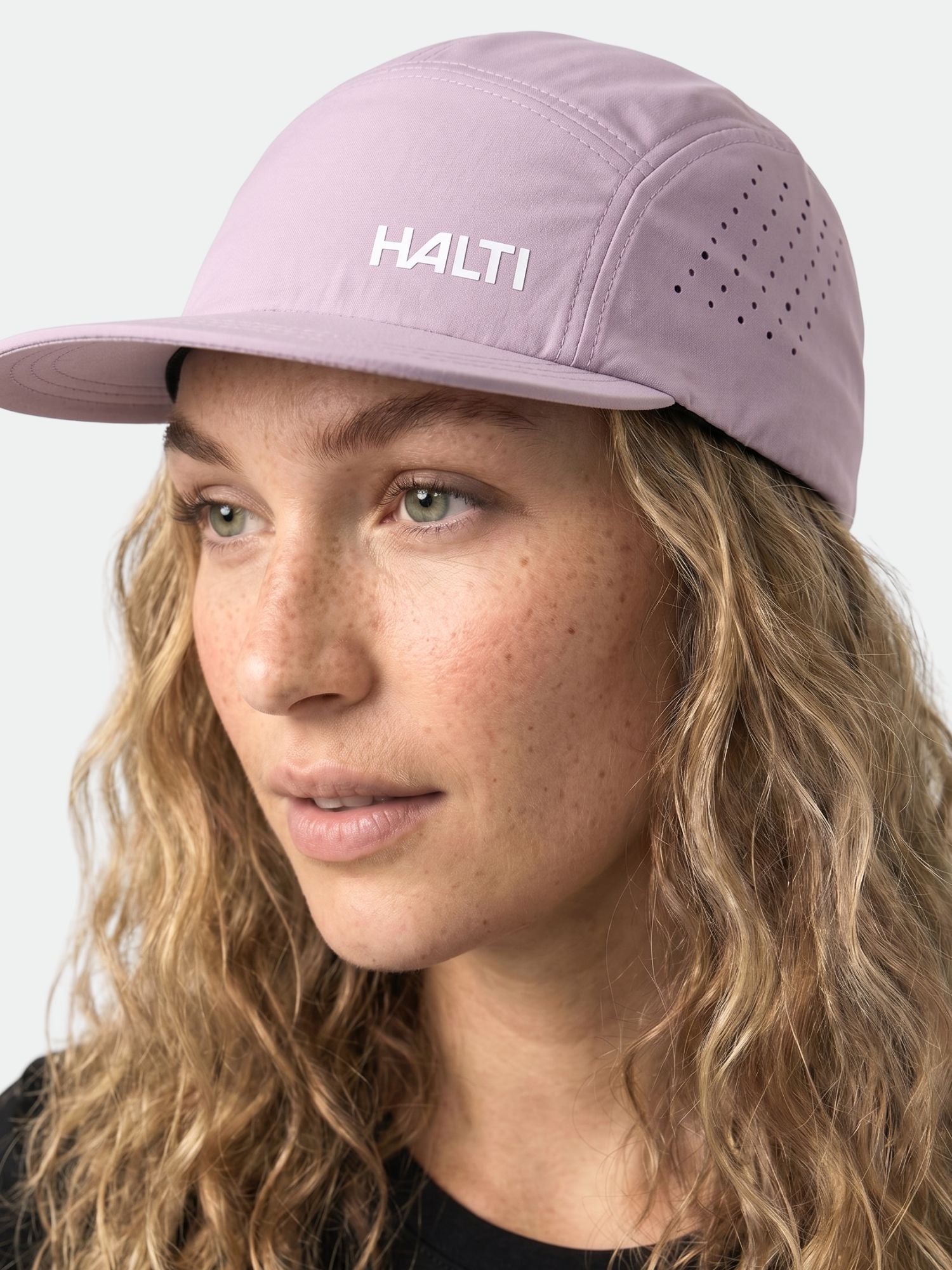 A person with wavy blonde hair wears a light purple Halti Luovi Cap with ventilation holes on the side.