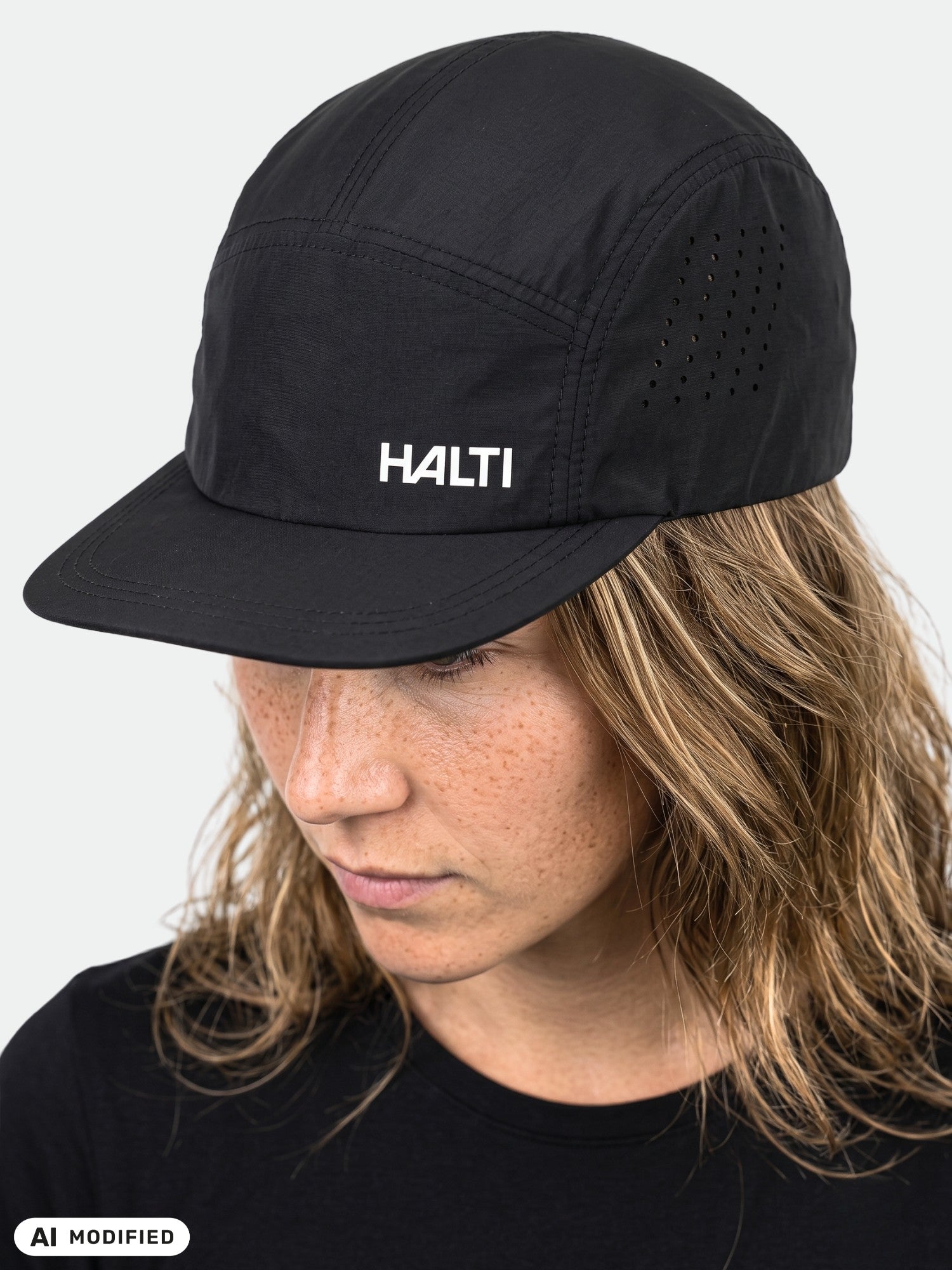 Person wears a black Halti Luovi Cap and shirt, looking downward against a plain light background.
