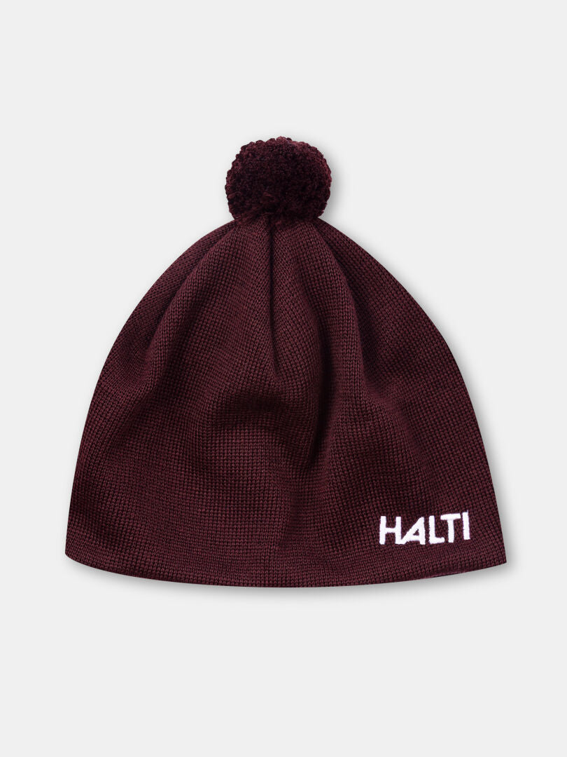 The Peesi II Beanie by Halti is maroon, knit, features a pom-pom, and has HALTI embroidered in white on the front.