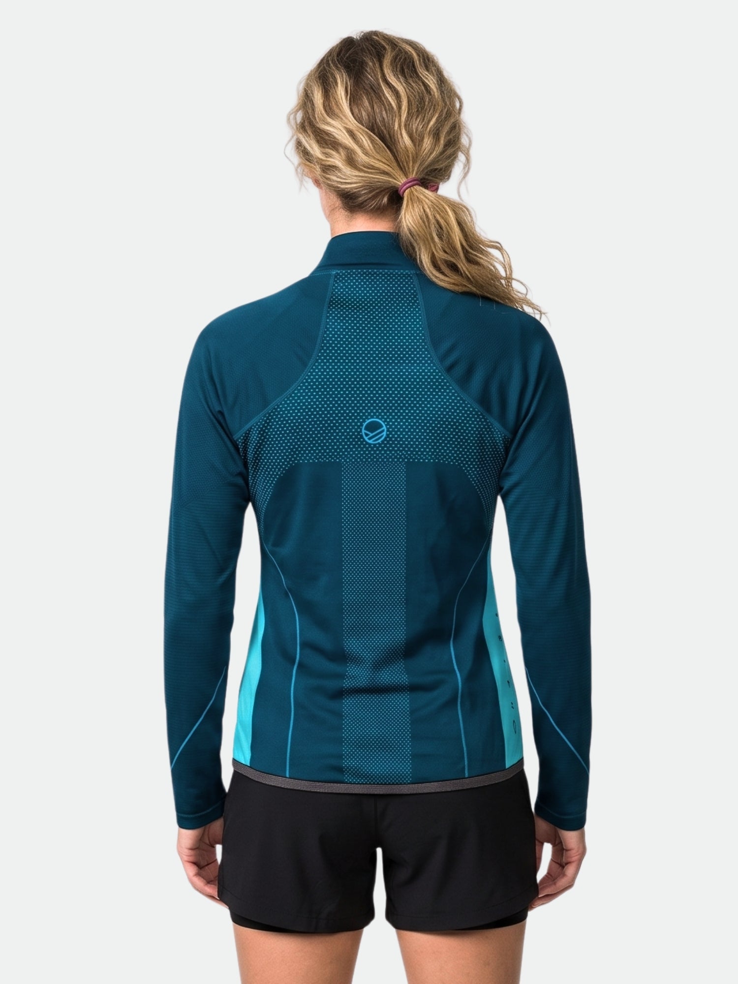 A woman with wavy blonde hair wears Halti's Tracks Women's Seamless Jacket in blue and black shorts, back view on white.