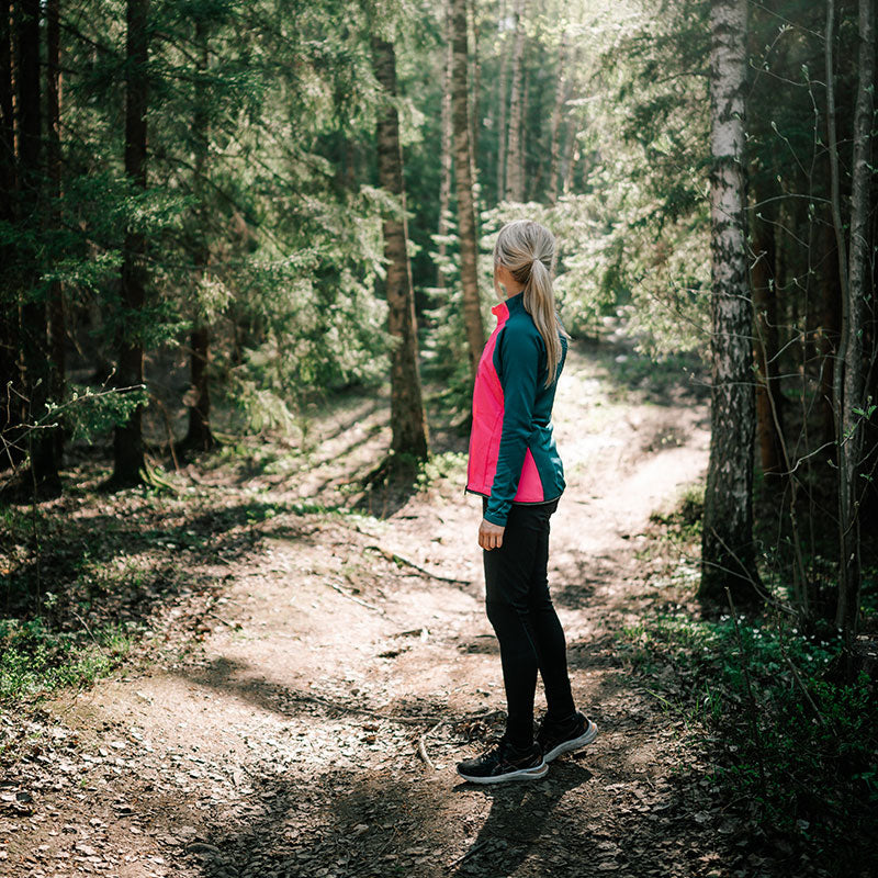 Person with blonde hair stands on a dirt trail wearing Halti Tracks Womens Seamless Jacket and black pants.