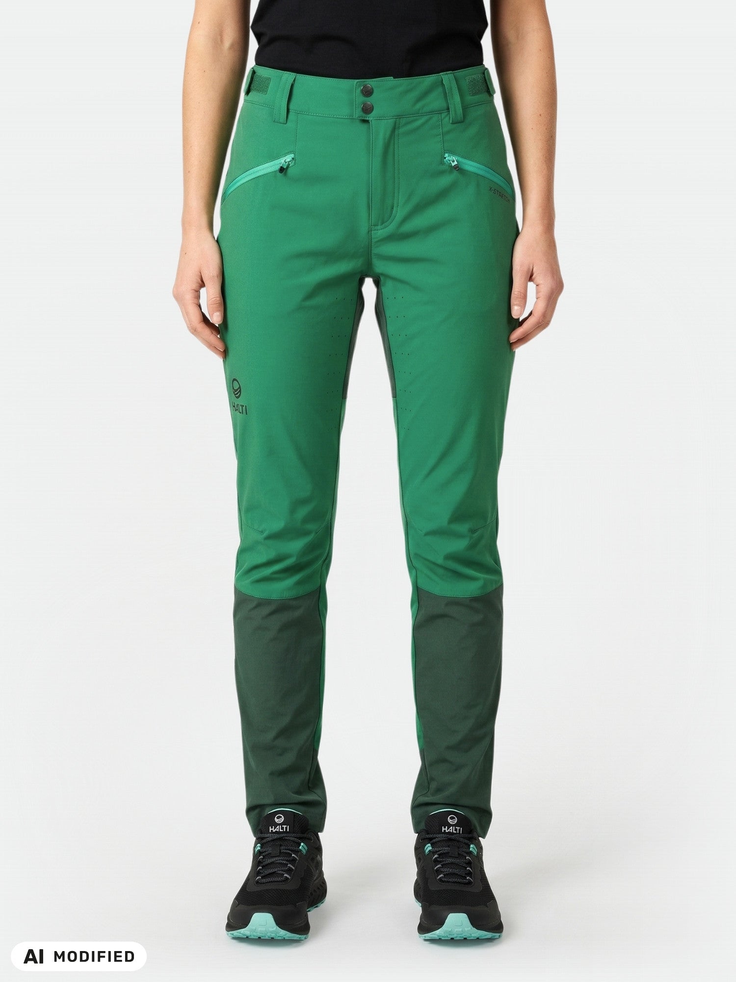 Woman wearing Halti Tracks X-stretch Pants in green, black shirt, and black shoes against a plain background.