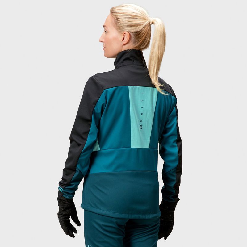 A woman with blonde hair in a ponytail wears the Halti Vinha XCT Jacket Womens, facing away from the camera.