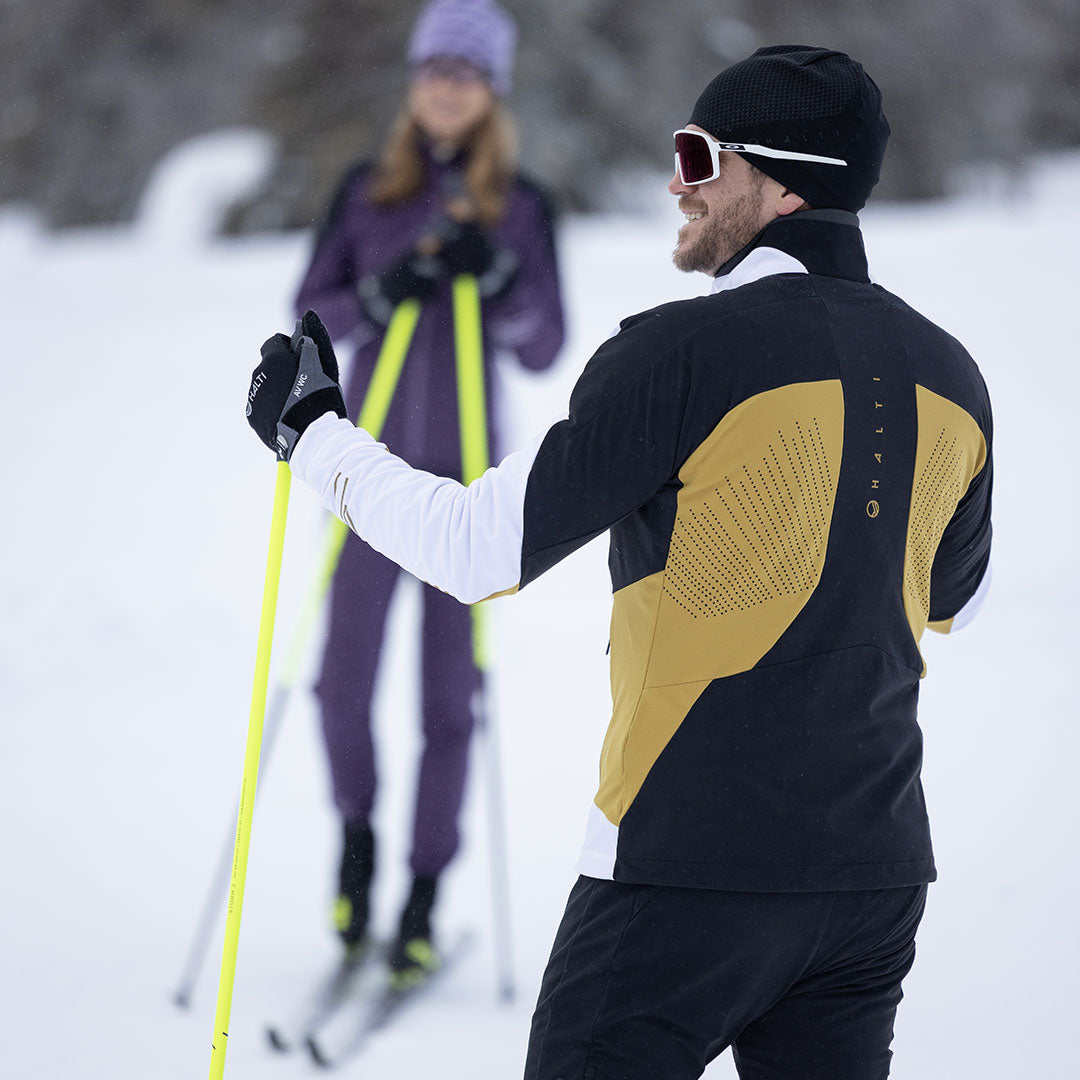 Two cross-country skiers on snow; one wears the Halti Veloce XCT Jacket Mens, a breathable, high-performance layer.