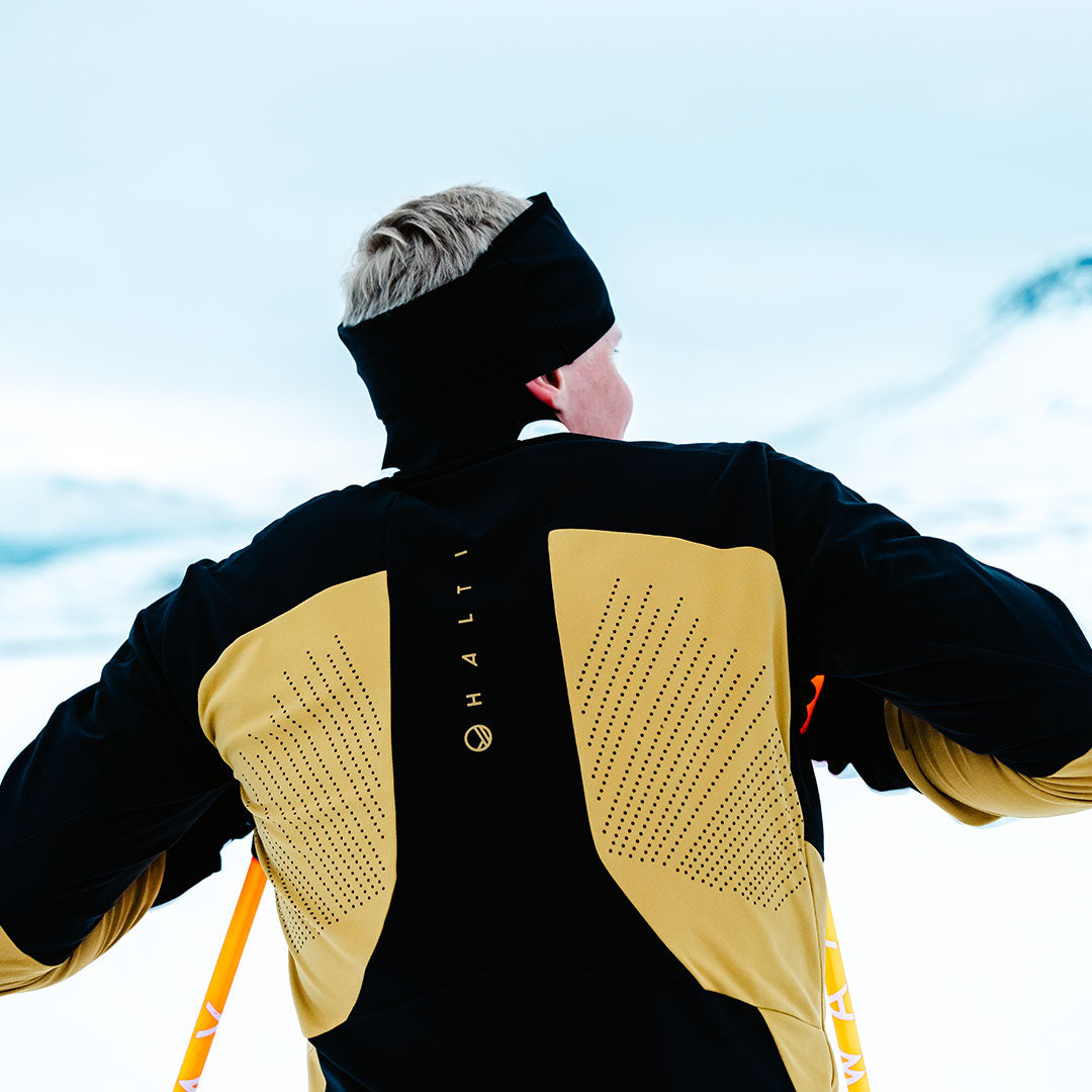 Wearing the Halti Veloce XCT Jacket Mens, a skier stands with skis in a snowy landscape, facing away.