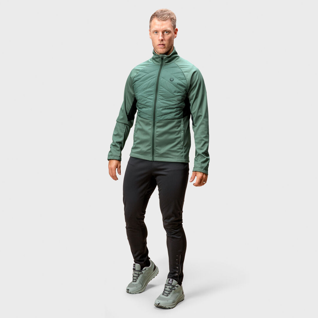 A man in a green Halti Vinha Hybrid XCT Jacket, black pants, and green sneakers stands against a grey background.