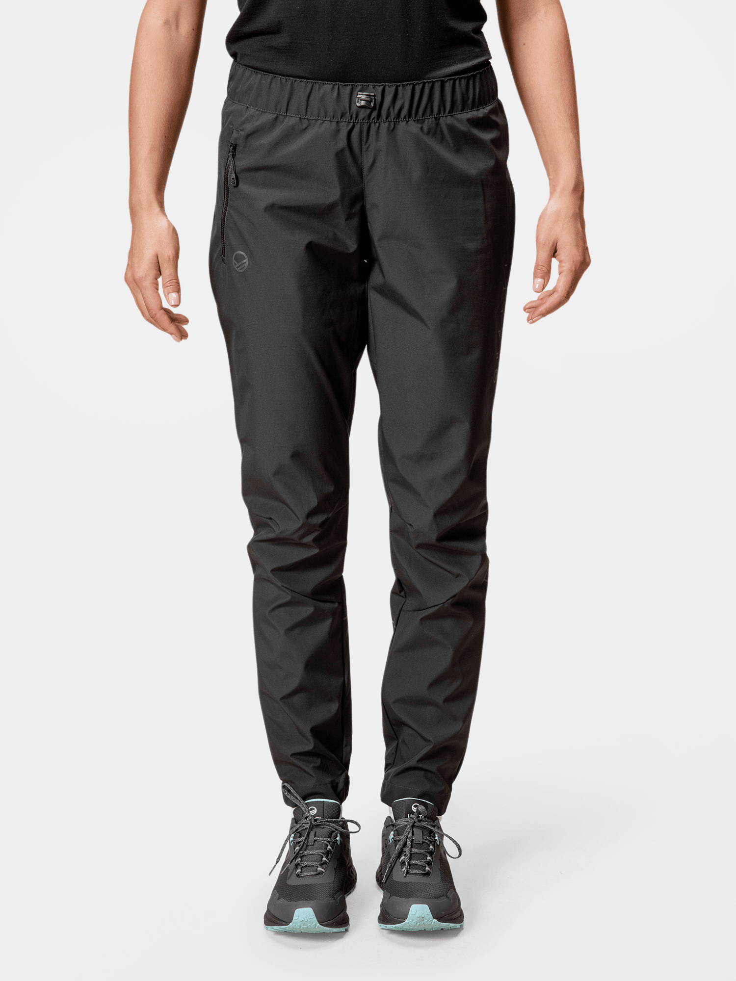 A person faces forward in Halti Shelter Stormwall 3L Pants and black sneakers with light green accents against a plain background.