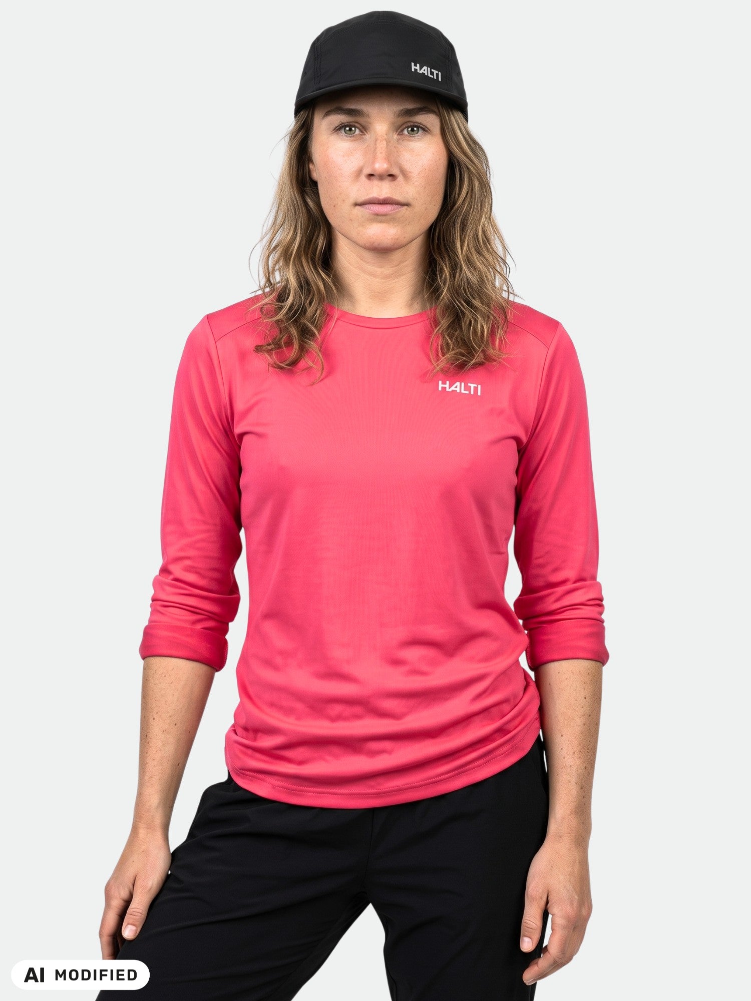 A woman in a pink Halti Salves Training Shirt, black pants, and cap stands against a plain white background.