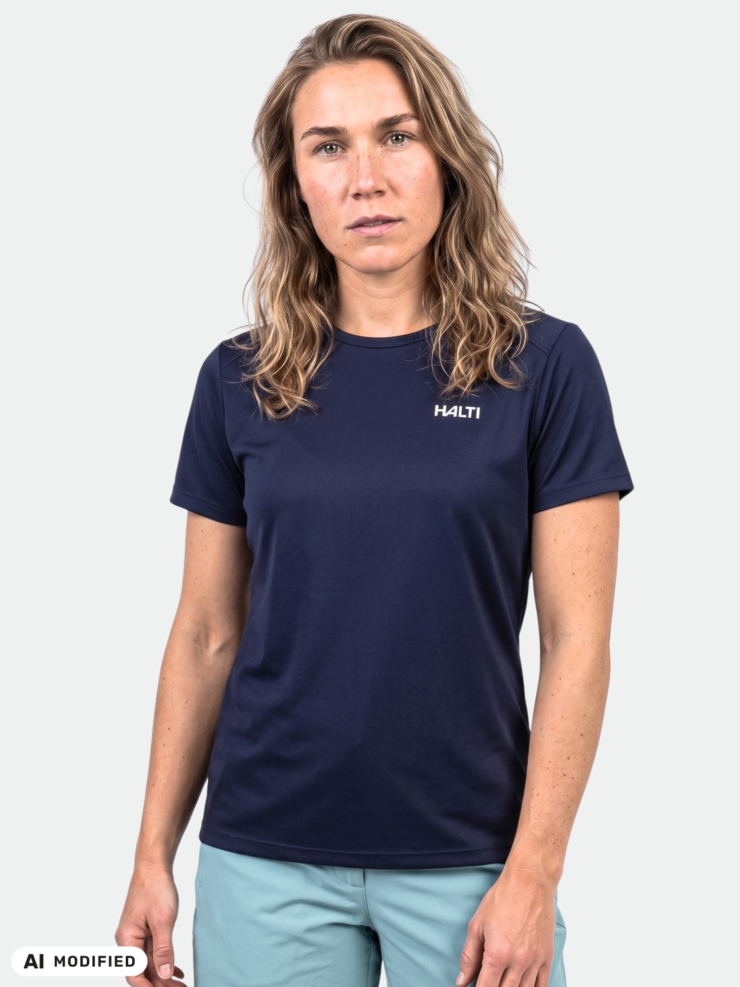 A woman with wavy hair wears a navy Halti Salves T-shirt and light blue shorts against a white background.