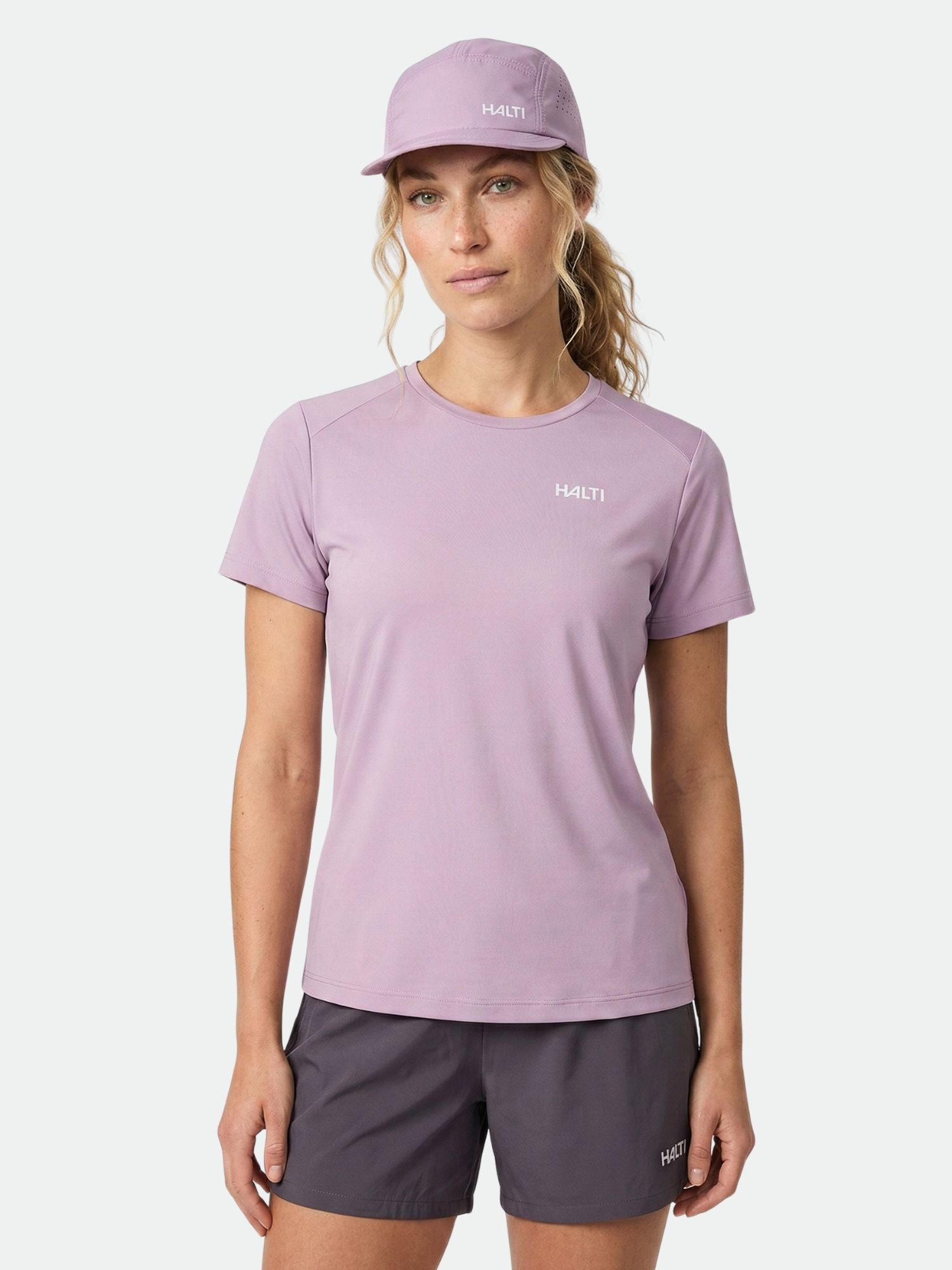 Woman wearing a Halti Salves T-Shirt Women's in light purple, matching cap, and dark shorts on a plain white background.