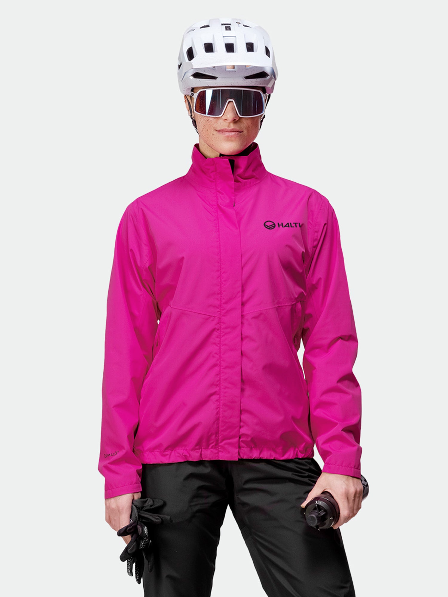 Woman wearing a Halti Triant DX Cycling Jacket in bright pink with reflective details, black pants, helmet, and sunglasses.