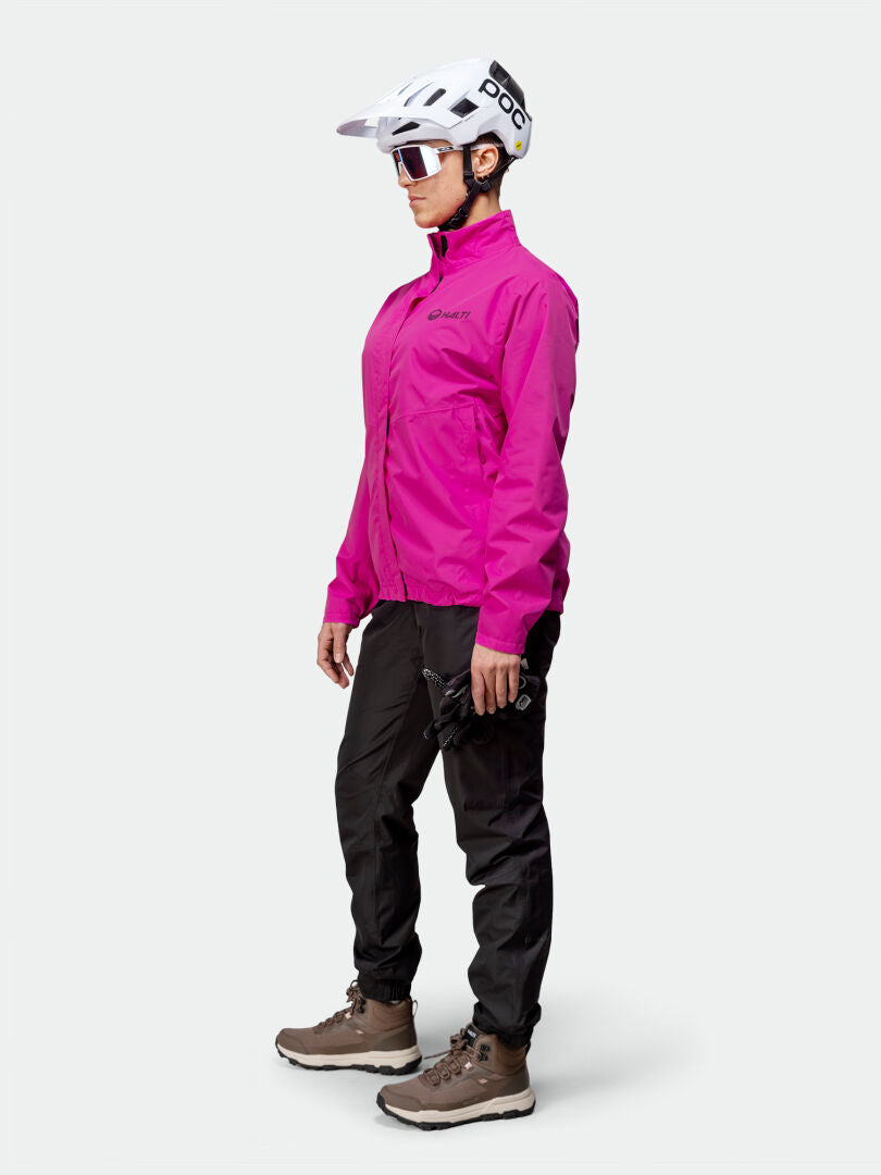 A woman wearing the Halti Triant DX Cycling Jacket, white helmet, sunglasses, black pants, and brown boots.