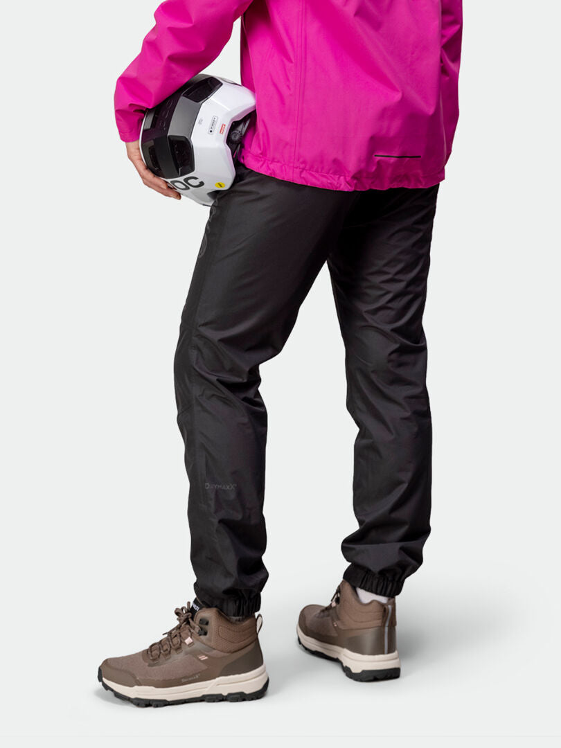 Wearing Halti Triant DX Cycling Pants, a woman in hiking boots and a bright pink jacket holds a white helmet.