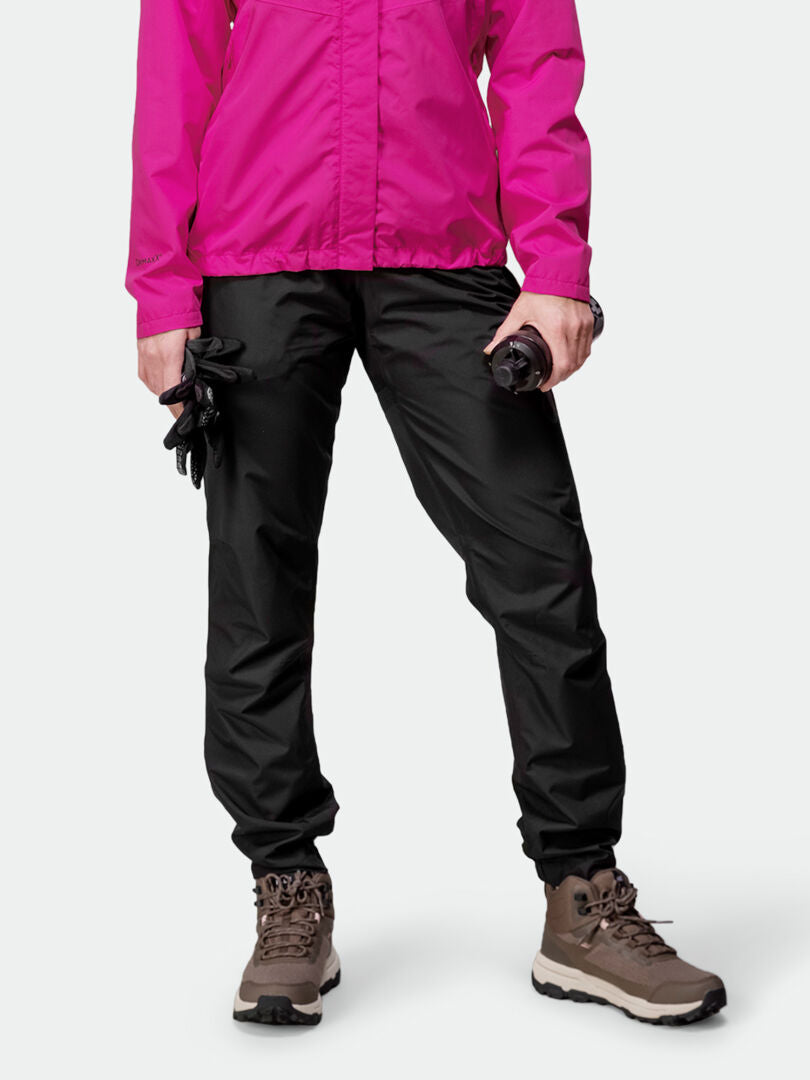 Person in a bright pink jacket, Halti Triant DX Cycling Pants Womens, brown hiking boots, holding gloves and water bottle.