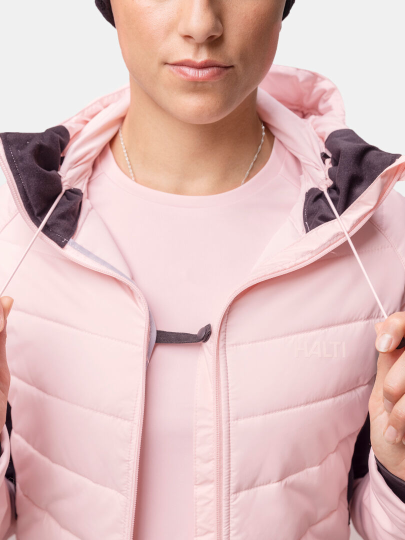 A woman in a light pink Halti Hanki 2 Hybrid XCT Jacket pulls the hood cords, showing the logo on the chest.