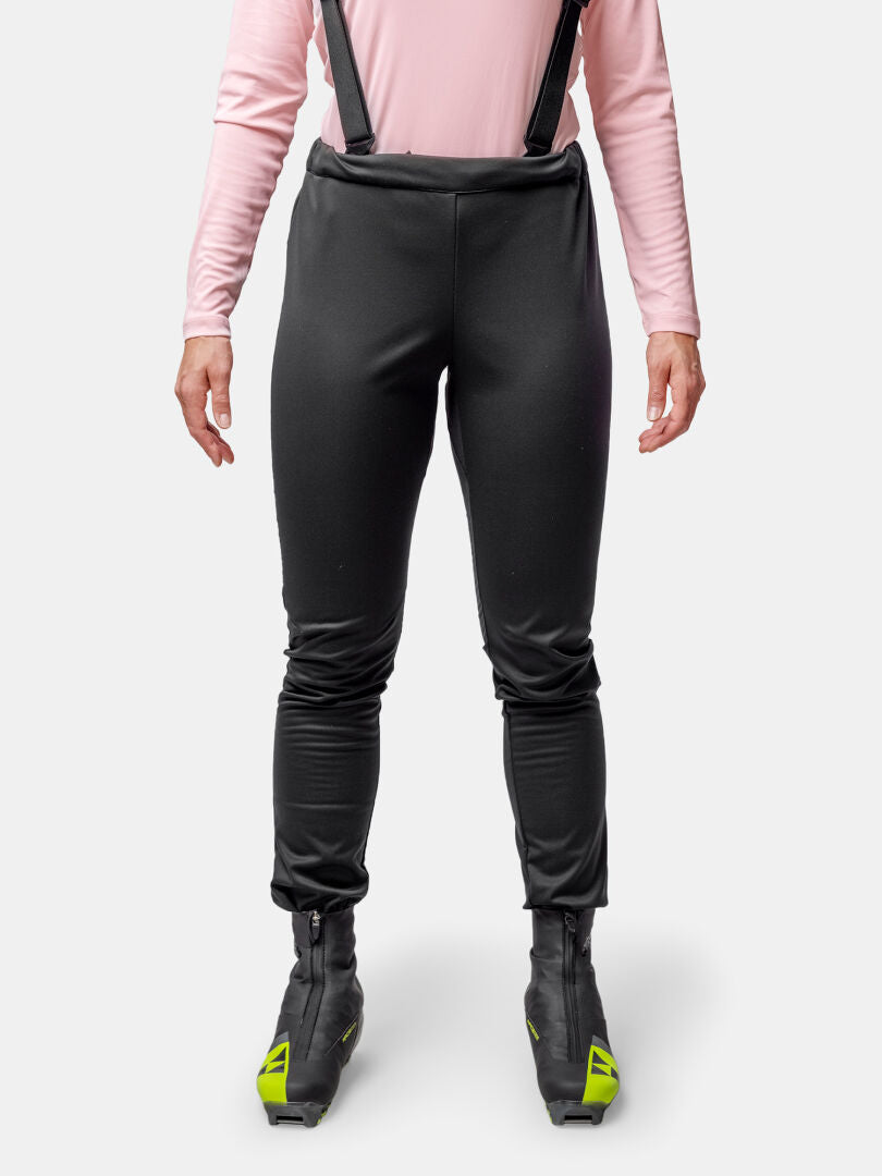 Woman in Halti Huuru XC Set: black ski pants with suspenders, pink long-sleeve top—ideal for winter training.