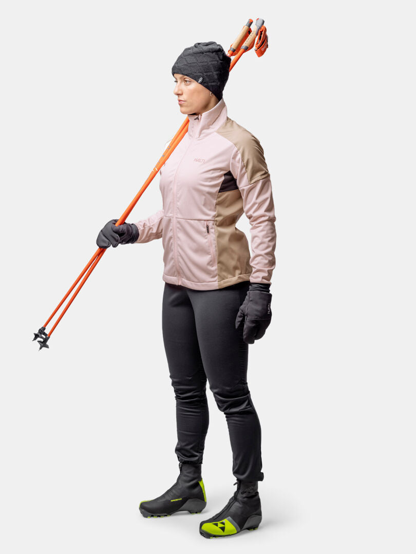 A woman in the Halti Huuru XC Set holds orange ski poles, ready for winter training against a plain white background.