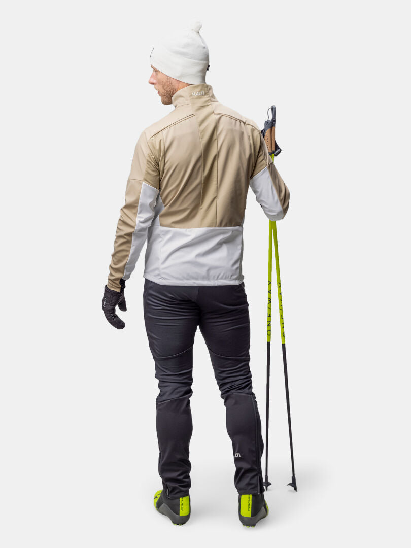 A person in the Halti Framover Hybrid XCT Jacket stands with ski poles, facing away on a plain white background.