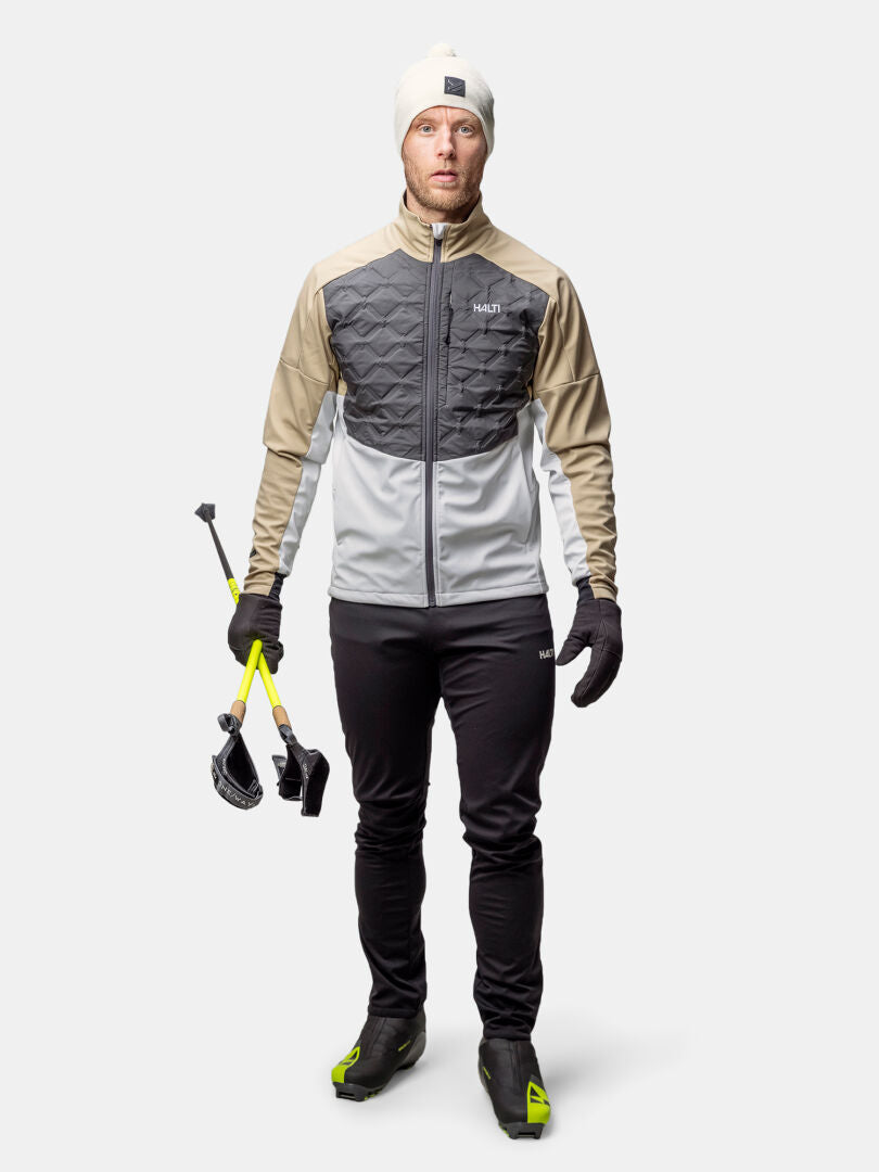 A man in the Halti Framover Hybrid XCT Jacket holds ski poles against a light grey background.