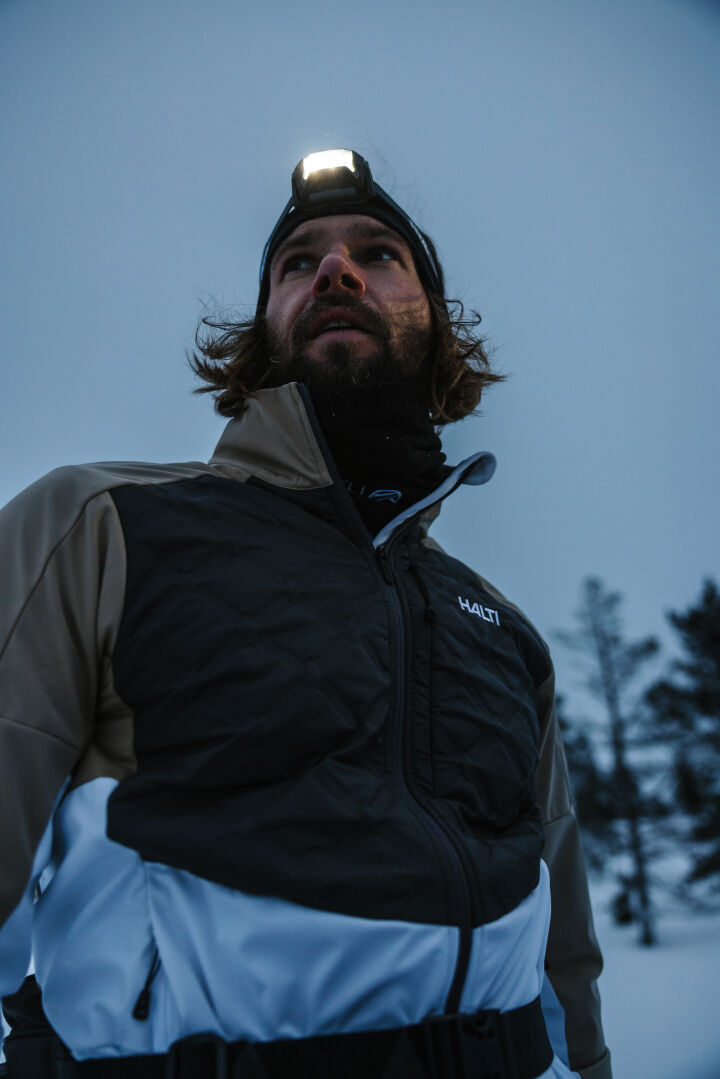 Wearing the Halti Framover Hybrid XCT Jacket and a headlamp, a man stands in snowy woods ready for winter workouts.