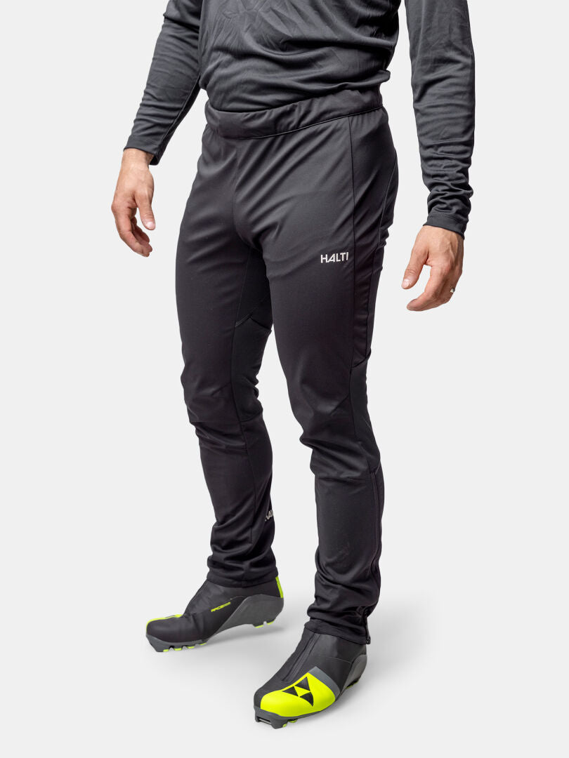 A person wears Halti Framover XCT Pants Men's, a long-sleeve shirt, and black shoes with yellow accents.