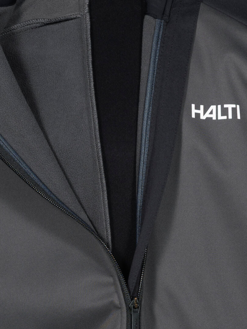 Close-up of Halti Huuru XC Set Men's dark gray windproof jacket with logo on chest and visible inner lining.