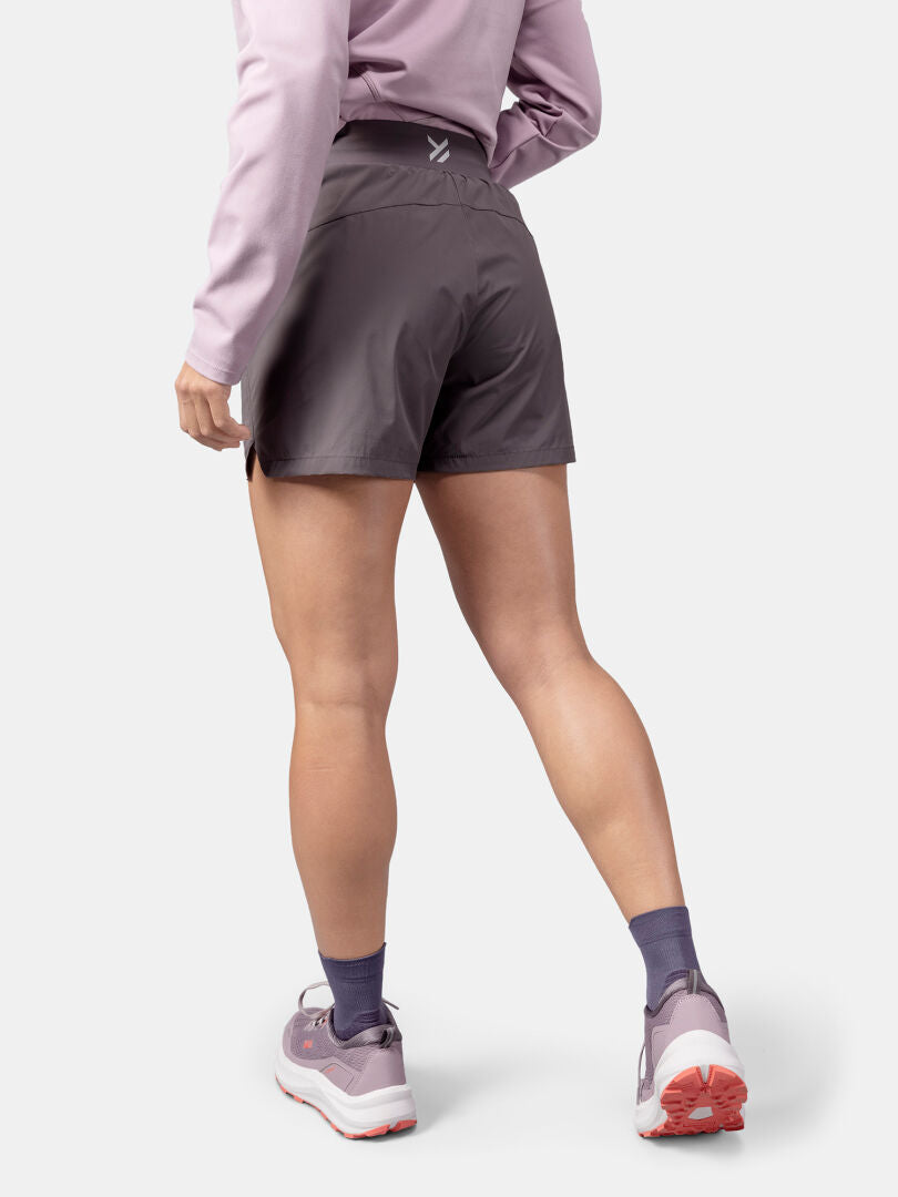 Person stands with their back to the camera, wearing Halti Uurto Shorts Women's and a pink top, purple socks, pink sneakers.