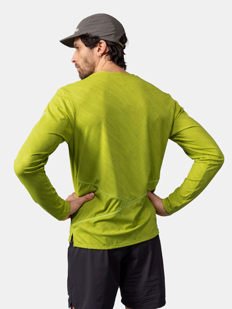 A man in a green Halti Oulanka Training Shirt, black shorts, and gray cap stands with hands on hips, facing away.