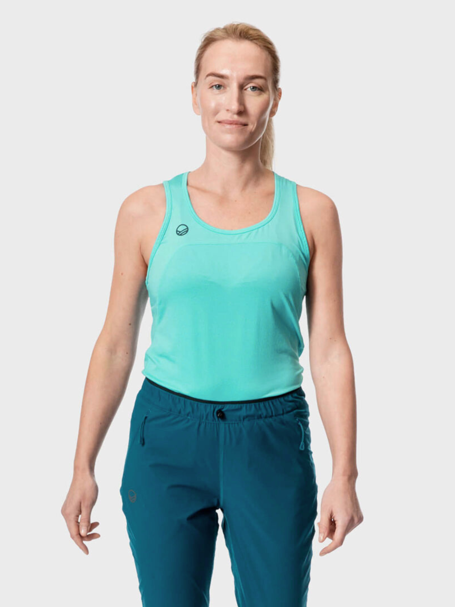 Wearing the Halti Urbanite Womens Active Dry Top and teal pants, she stands against a light gray background.