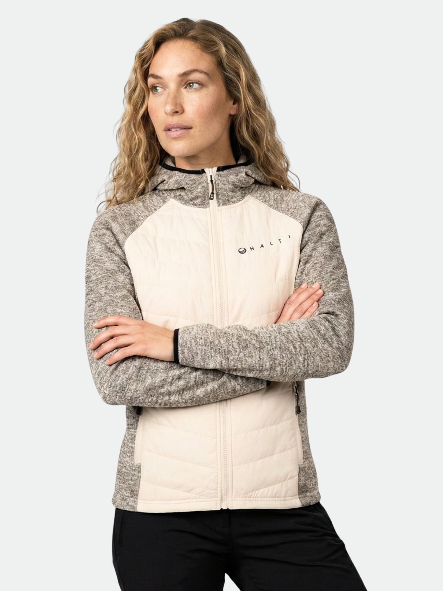 A woman in the Halti Streams Hybrid Layer Jacket stands with arms crossed against a plain background.