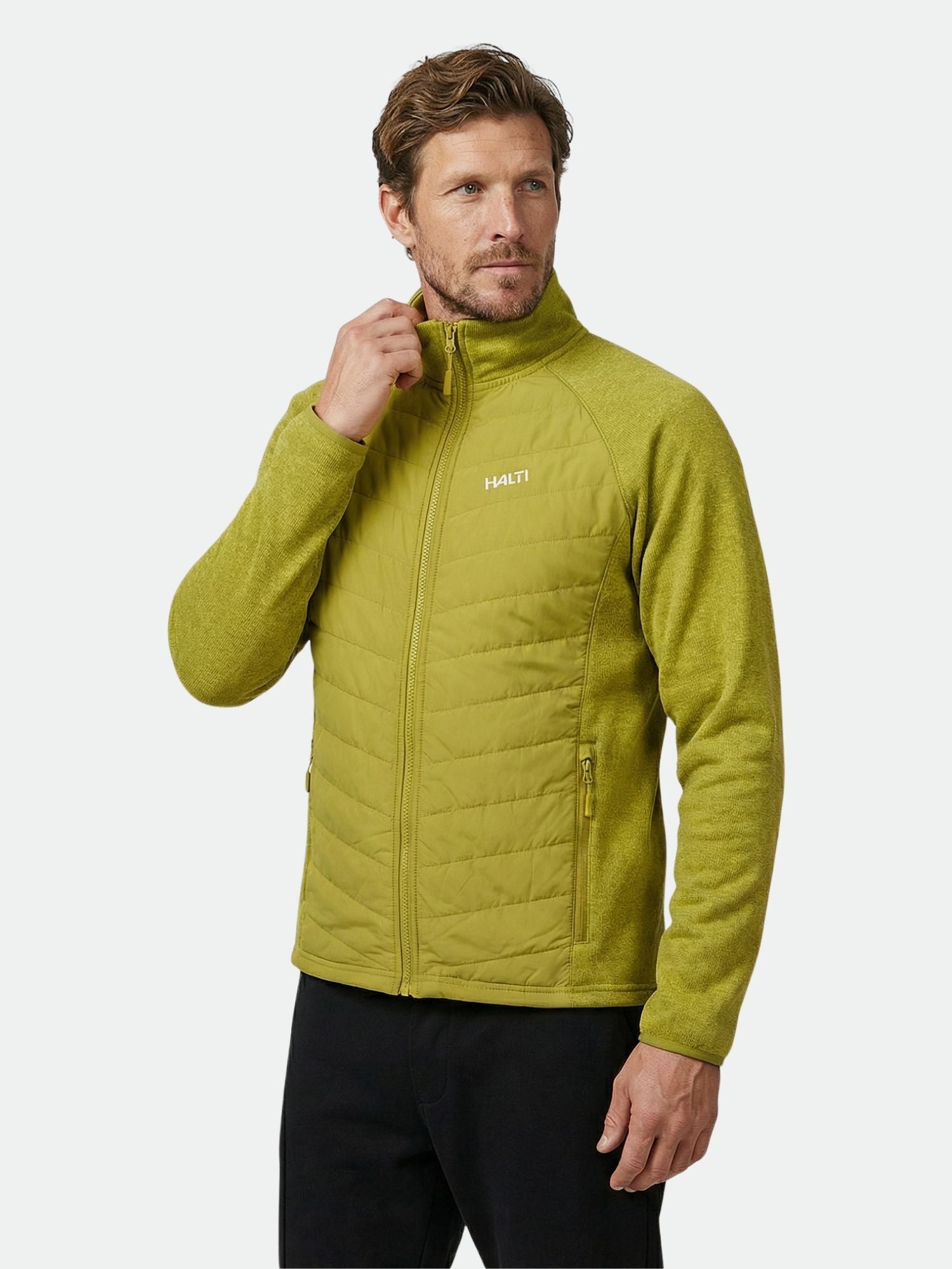 A man wears a Halti Streams Hybrid Layer Jacket Men's in light green with black pants, standing slightly sideways.