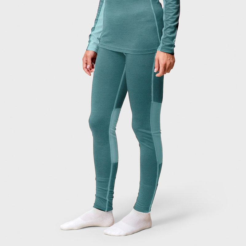 Woman in Halti Pihka II Merino Baselayer Pants stands on white surface in white socks, hands at sides.