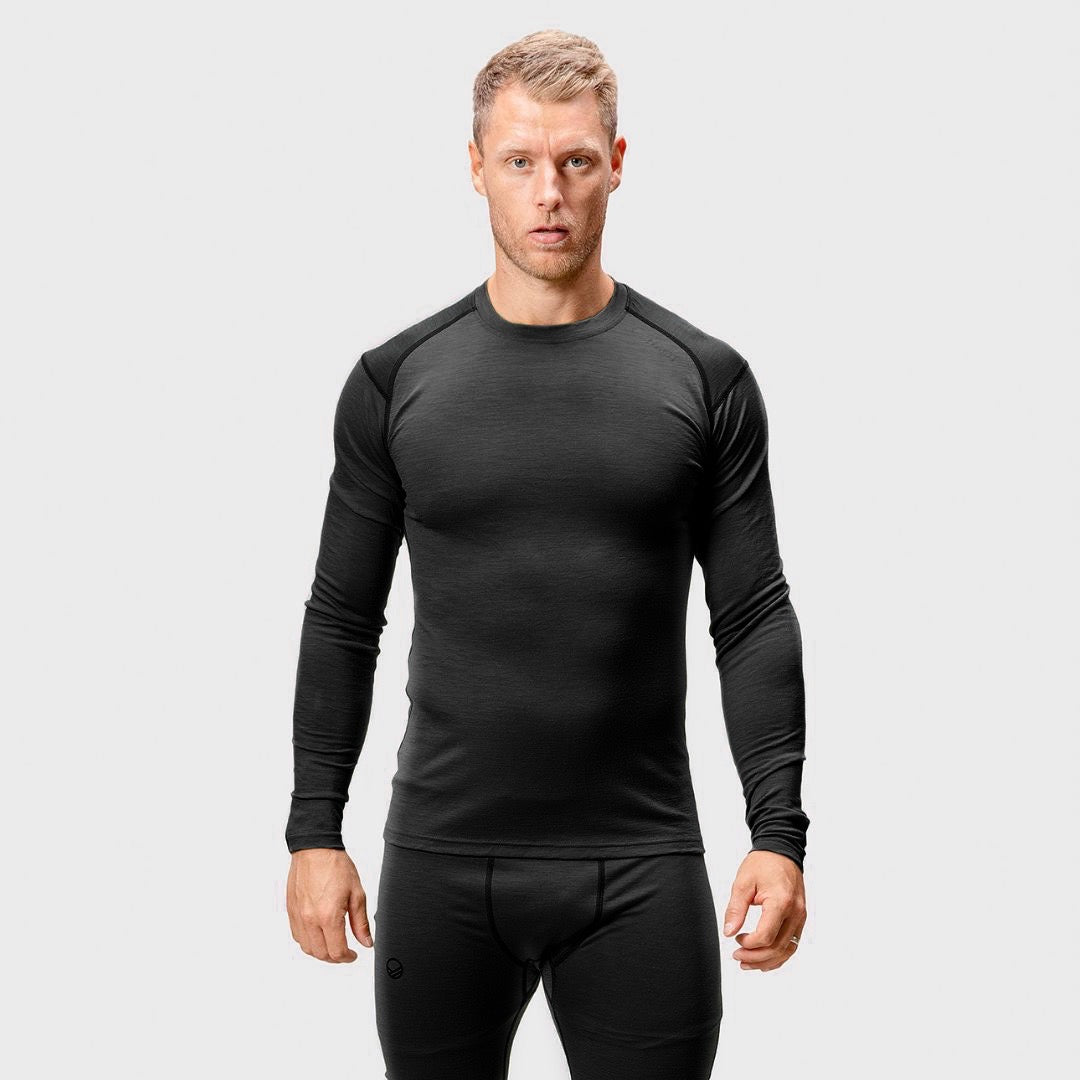 A man wears a fitted Halti Pihka II Merino Baselayer Shirt for men, standing against a plain light gray background.
