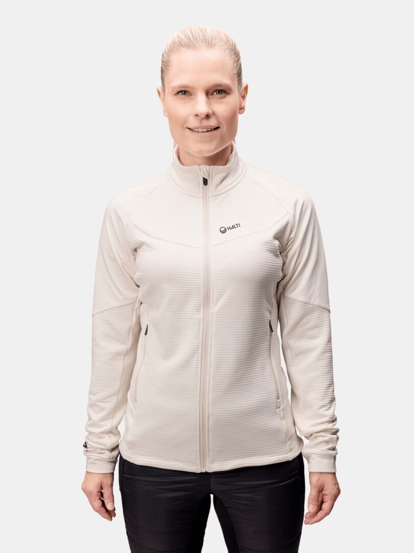 A person with light hair in a ponytail wears the Halti HeatGrid Layer Jacket Women's and black pants against a plain background.
