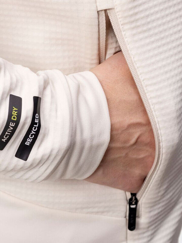 A person’s hand is in the pocket of a Halti HeatGrid Layer Jacket Women’s featuring “ACTIVE DRY” and “RECYCLED” labels.