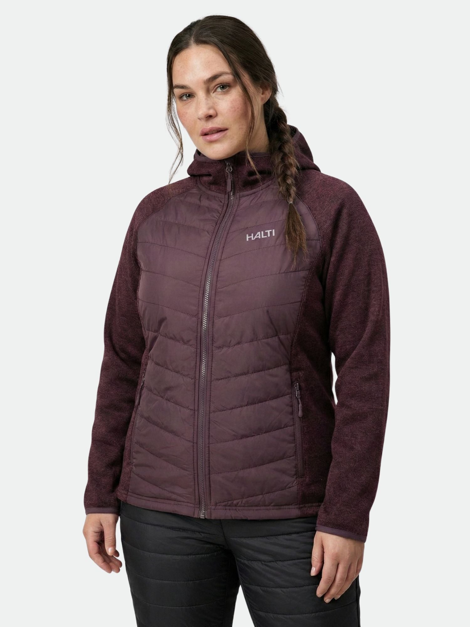 A woman in a maroon Halti Streams Hybrid Layer Jacket Women's Plus and black pants stands against a plain background.