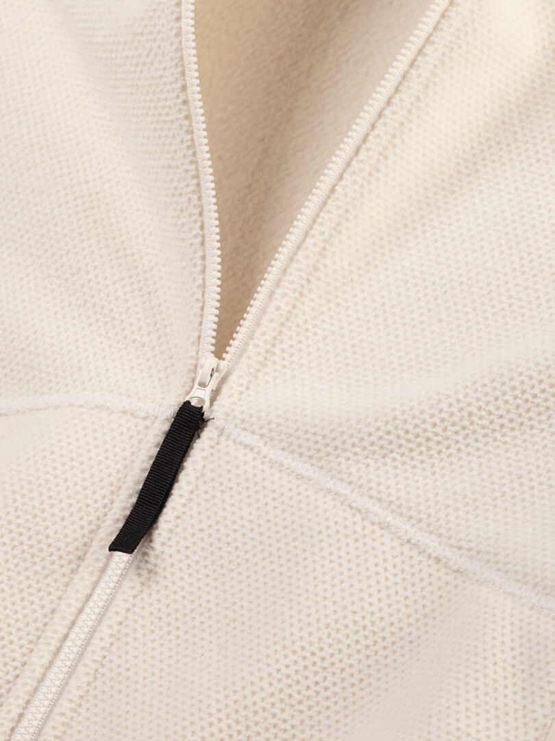 Close-up of a partially unzipped Halti Soolo Layer Jacket Women's with textured white fabric and black zipper pull.