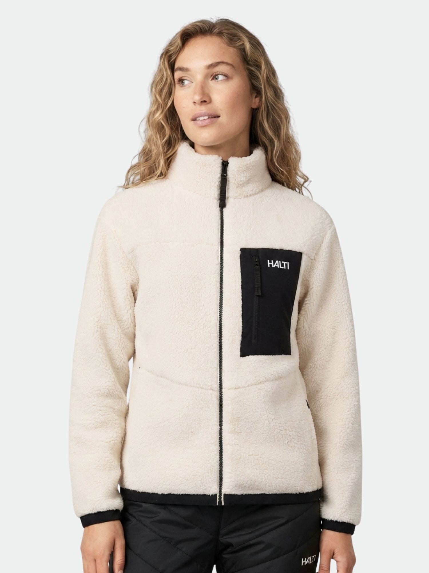 A woman wears the Halti Lumista Polar Fleece Jacket in white with a black chest pocket and logo, against a plain background.