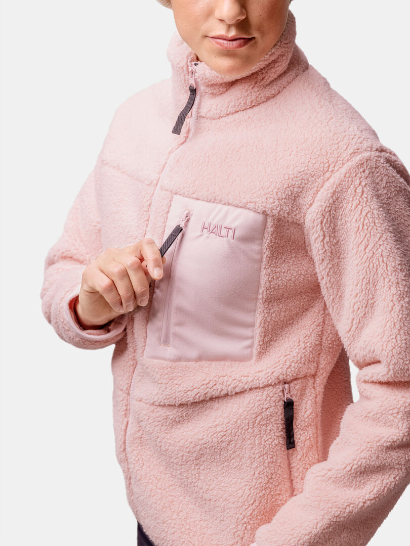 A woman in a light pink Halti Lumista Polar Fleece Jacket opens the zippered chest pocket.