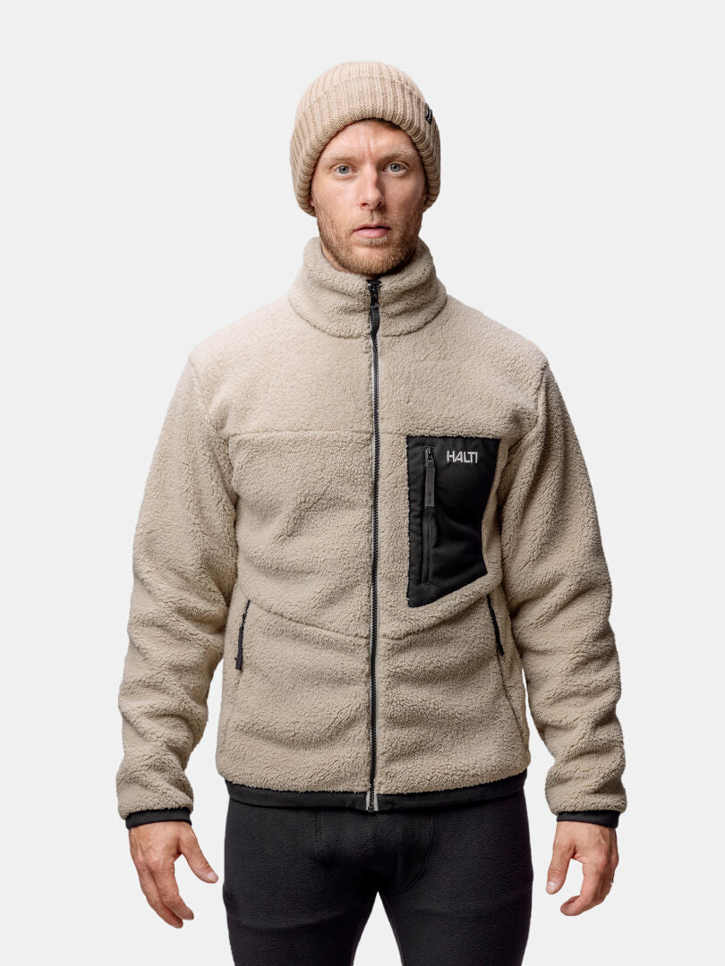 A man wears the Halti Lumista Polar Fleece Jacket in beige with black zippers and a knit beanie against a plain background.