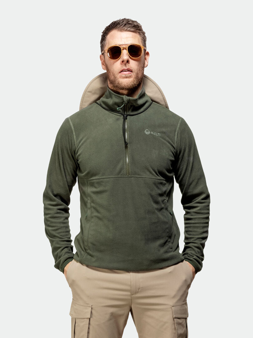 A man wears Halti Ossia Half Zip Fleece Shirt in green, sunglasses, and khaki cargo pants, hands in his pockets.
