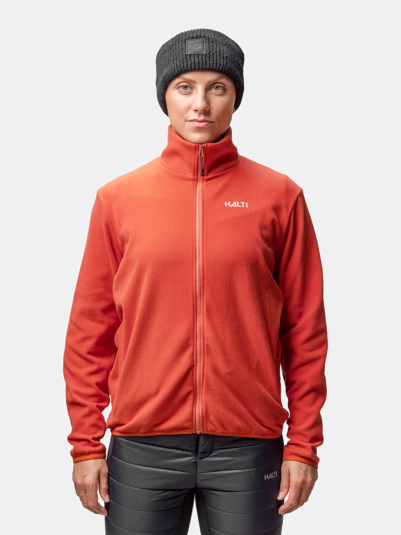 A person wears a Halti Rockmoon Fleece Jacket Womens in red, black pants, and a black beanie against a plain background.