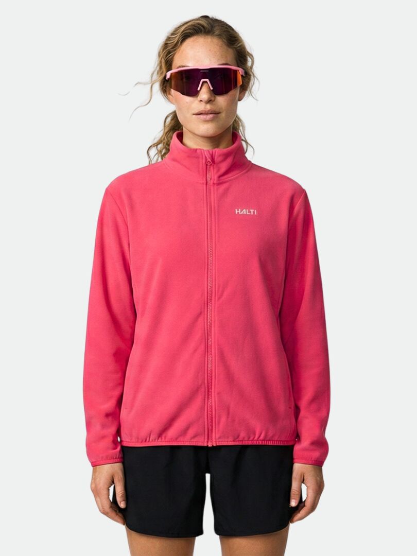 A person wears the Halti Rockmoon Fleece Jacket Women's in pink, black shorts, and large pink sunglasses against a plain background.