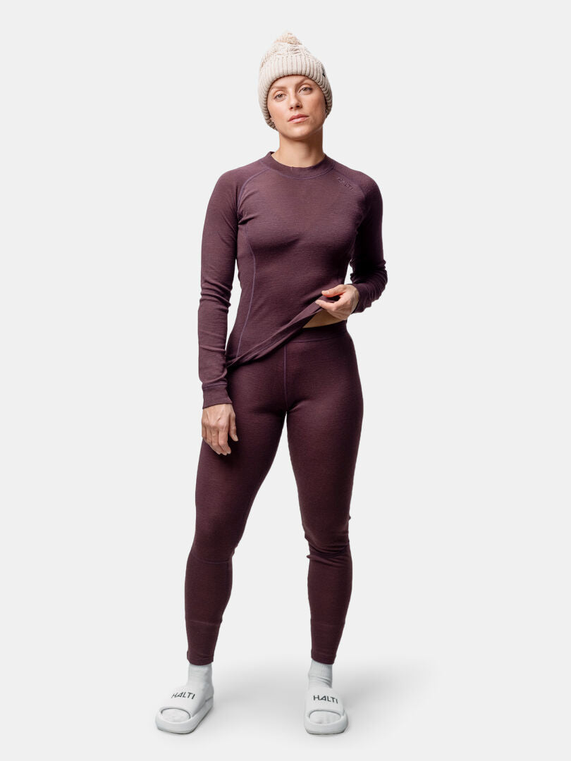 Woman wearing the Halti Hossa II Merino Base Layer Set, white slippers, and a beige knit hat stands against a light background.