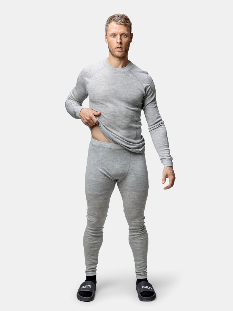 A man in the Halti Hossa II Merino Base Layer Set stands facing forward, lifting his shirt slightly with one hand.