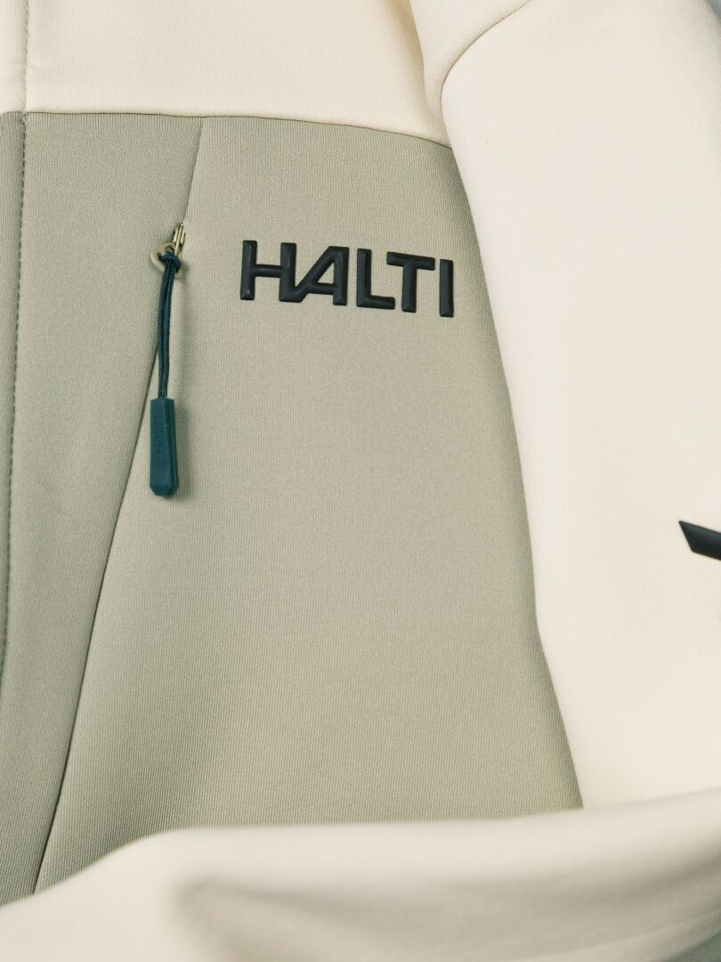 Close-up of a Halti Seiland Layer Jacket Women’s chest pocket with a zipper pull and the brand name printed in black.